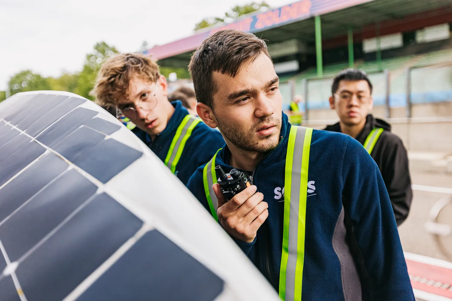 A team member holding a radio, looking down the pit lane, with the car's solar deck in the foreground.