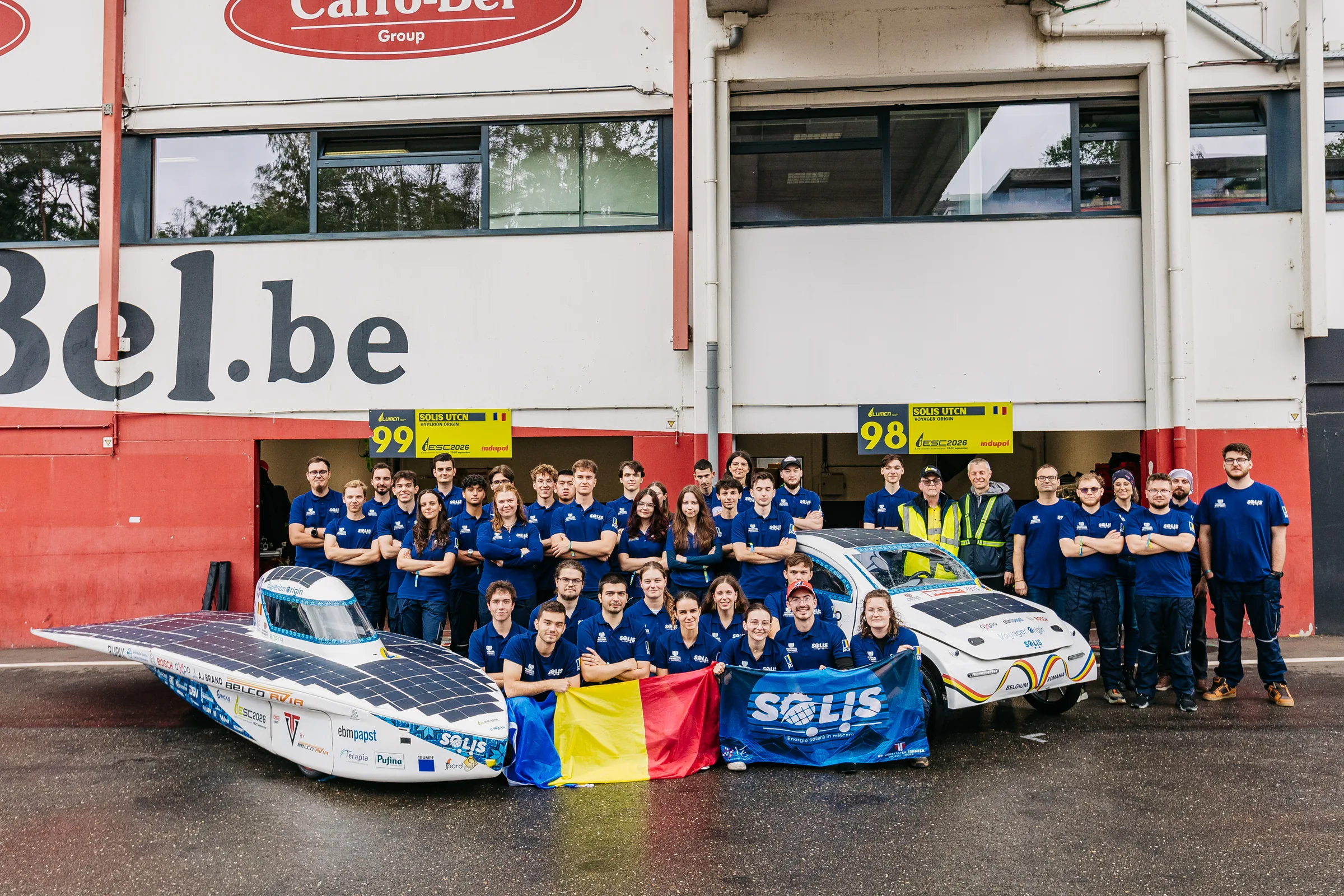 The whole Solis team in blue shirts with both cars and the Romanian flag, in front of the Zolder pit garages.