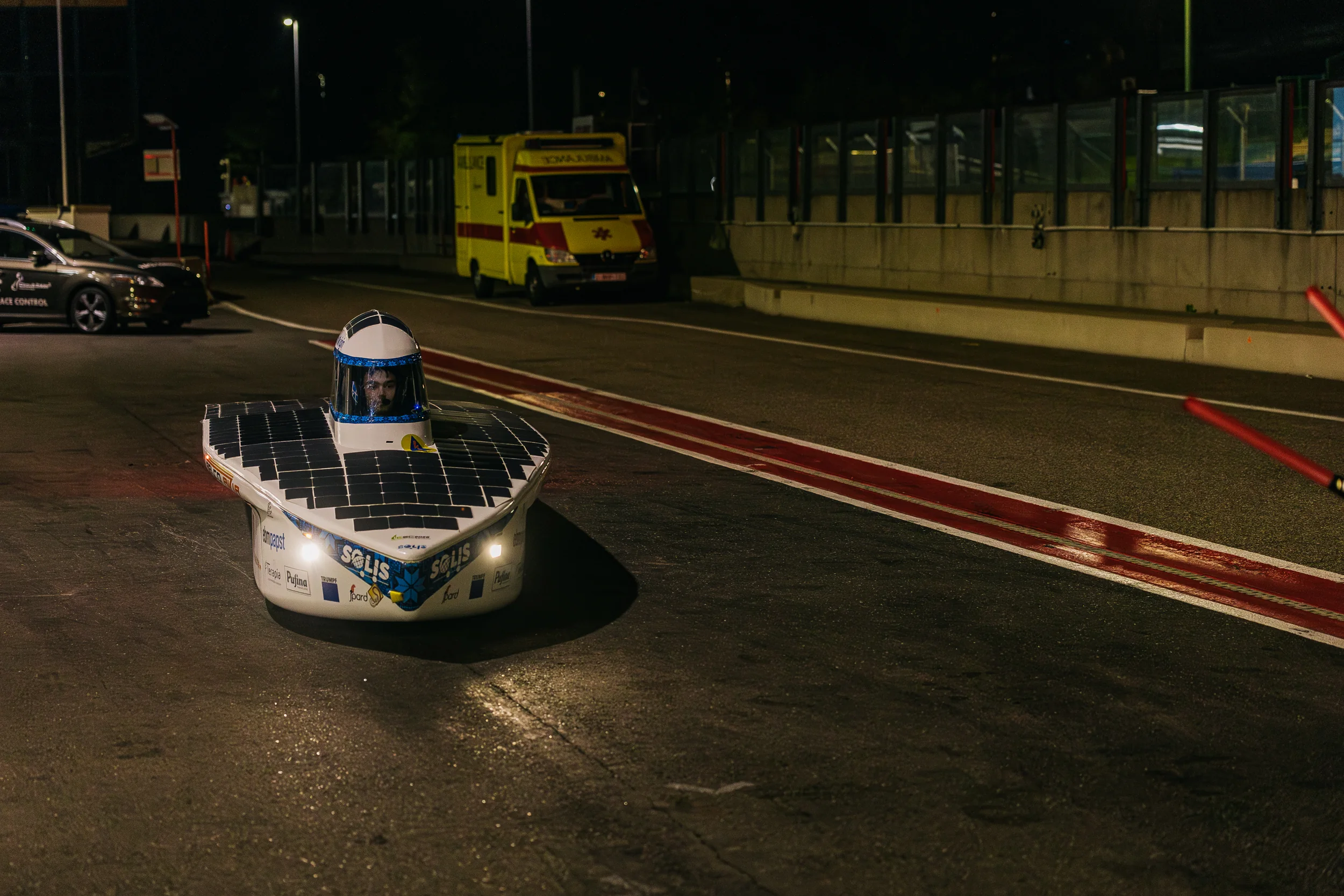 Hyperion Origin rolling down the pit lane at Circuit Zolder at night, headlights on, the driver's face lit inside the canopy.