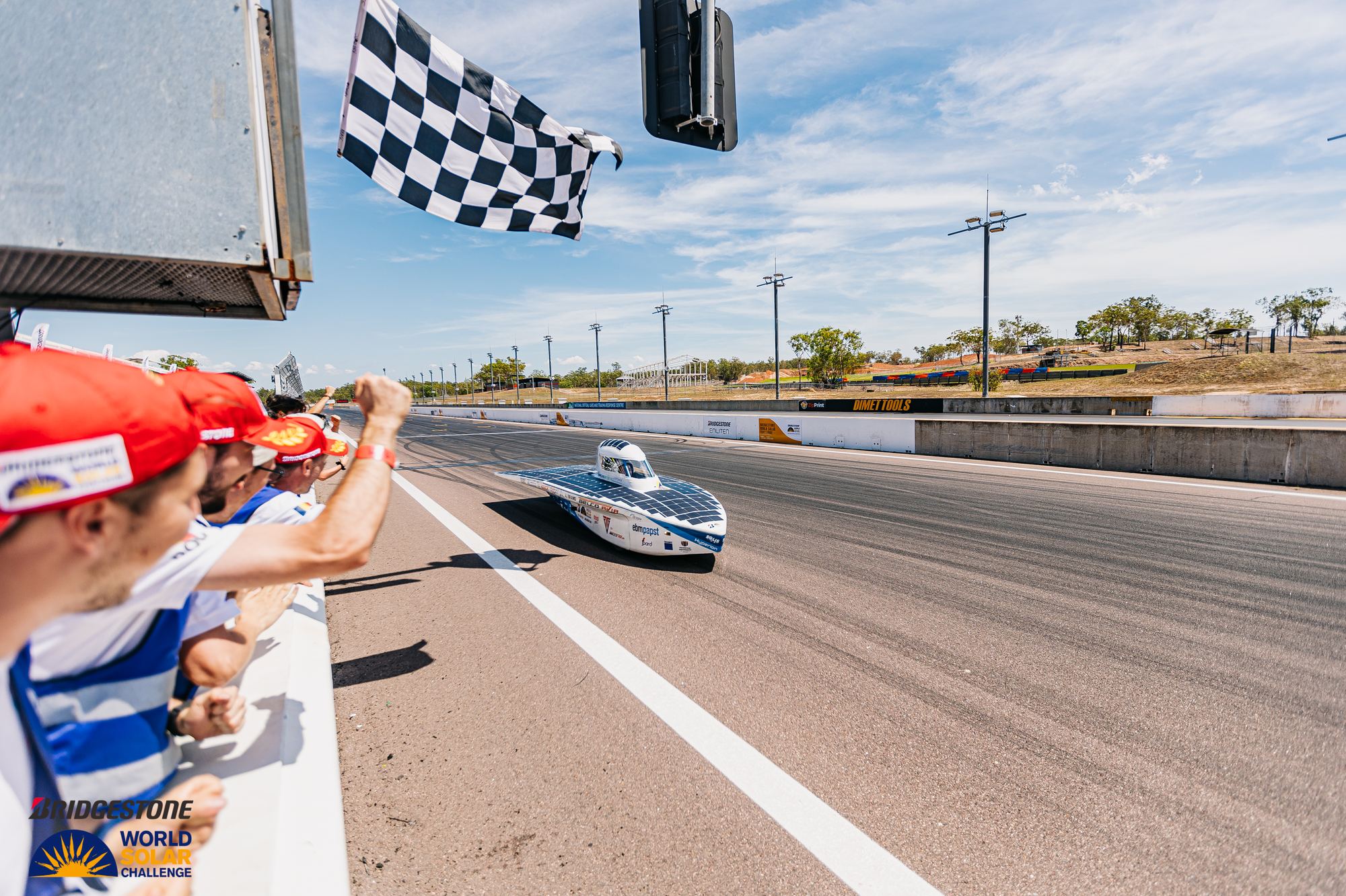 Hyperion passing the chequered flag at Hidden Valley, Darwin, with people cheering from the pit wall.